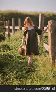 A red-haired girl is walking near a massive fence made of boards.. A beautiful red-haired girl is standing near a massive wooden fence 3246.