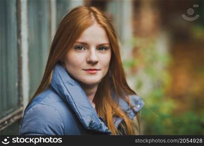 A red-haired girl near a brick wall.. A girl with long red hair is sitting on the windowsill of an old house 2736.
