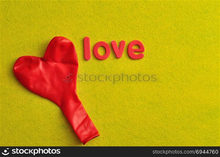 A red heart shape balloon and the word love on a yellow background