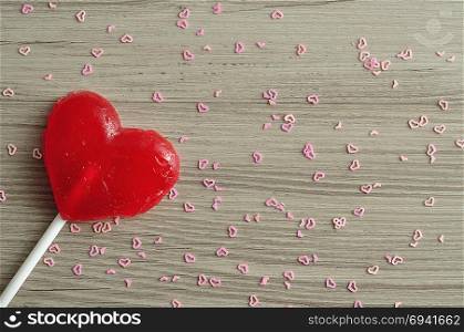 A red heart shape lollipop isolated against a wooden background with small pink hearts