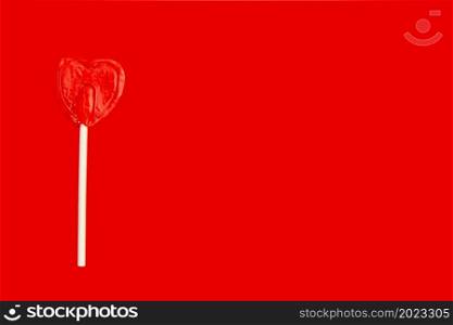 A red heart shaped lollipop on the left side of the image with copy space on a red background.. A red heart shaped lollipop on the left side of the image with copy space on a red background