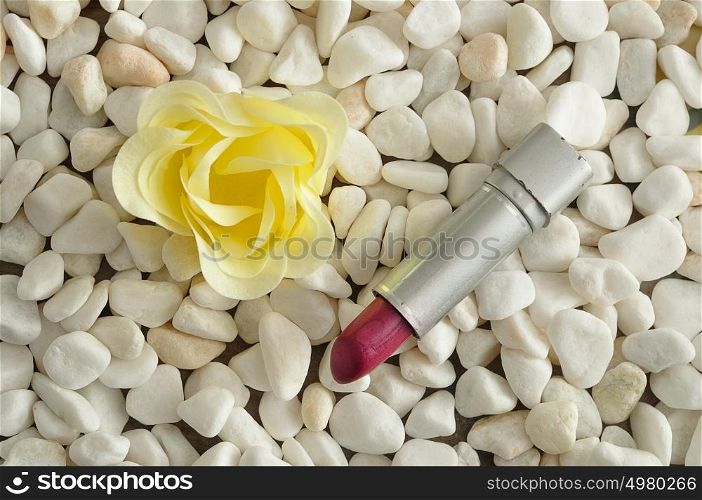 A red lipstick displayed on white pebbles with a white flower
