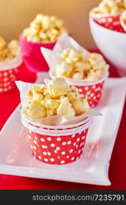 A red paper cup with popcorn against orange background with spot lighting,shallow Depth of Field,Focus on popcorn.. A red paper cup with popcorn.