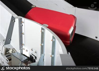 A red suitcase on an airport conveyor belt being transported to an airplane