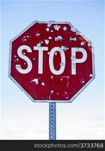 A red traffic stop sign riddled with bullet holes highlighted against a light blue sky.
