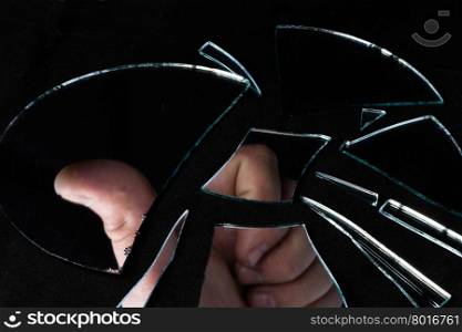 a reflection of the man&rsquo;s hand in pieces of broken mirror on a black background