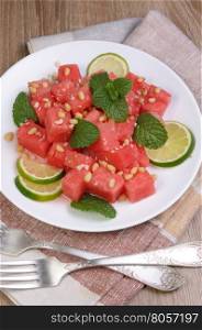 A refreshing salad of watermelon cubes with slices of lime, mint, peanuts, pine nuts
