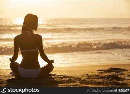 A relaxed sexy young woman or girl wearing a bikini sitting on a deserted tropical beach at sunset or sunrise
