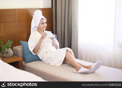 A relaxed woman wearing white bathrobe and towel having a coffee in the morning