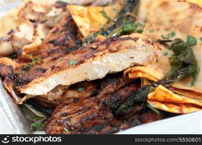 A restaurant tray of Turkish or Arab spatchcocked, marinaded grilled chicken, served with flat Arab bread with a tomato topping, chopped onion, sumac and coriander salad and grilled chilli peppers. The chicken has been sliced to show the texture