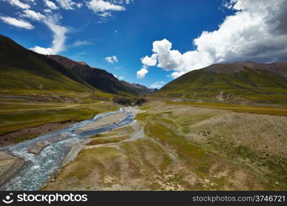 A river cross a plains in Tibetan Plateau, with mountain landscape and cloudy sky