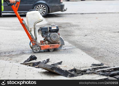 A road worker cuts with a gas cutter the destroyed old asphalt on the roadway for the subsequent repair of the road surface.. A petrol cutter cuts old asphalt with a diamond wheel, a road worker repairs the carriageway of a city road.