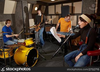 a rock band is working in studio. vocalist girl is singing with text of song in the her hand