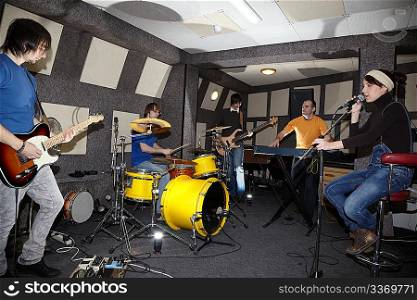 a rock band. vocalist girl, two musicians with electro guitars, keyboarder and one drummer working in studio. flashes in center