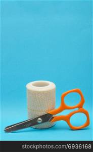 A roll of plaster with a scissor isolated on a blue background