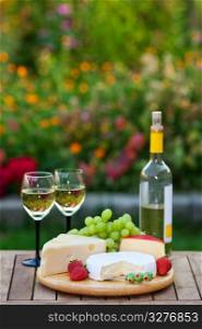 A romantic garden party for two, with white wine and an assortment of fruits and cheeses. Shallow depth of field.