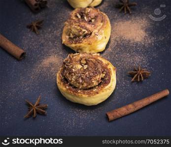 a round bun with cinnamon and nuts on a black background sprinkled with powdered cinnamon