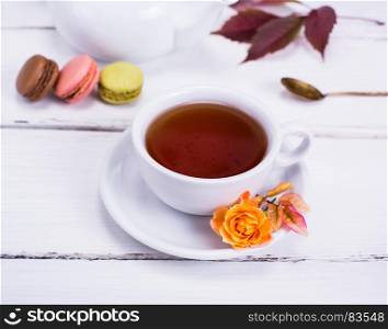 a round white cup with black tea on a white wooden table, behind three cakes, macarons