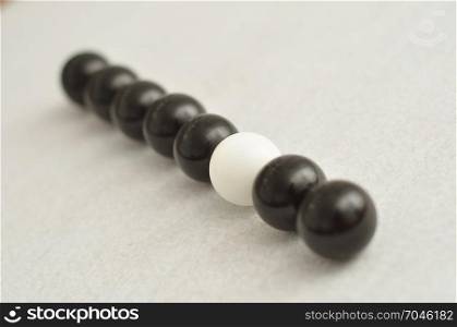 A row of black and white balls displayed on a white background, where by only the white one is in focus