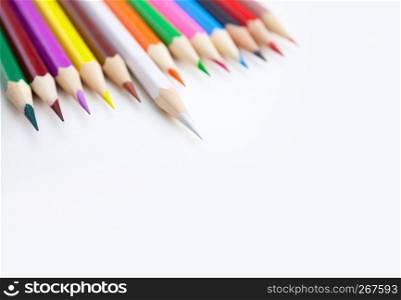 A row of colored crayon pencils on the white desktop with selected focus on the white color tips with copy space. Top view, closeup.