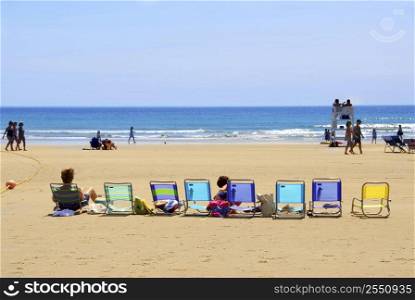 A row of colorful folding chairs on a sandy beach