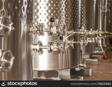 A row of fermentation tanks in a winery showing the valves and knobs used to control the flow of wine.