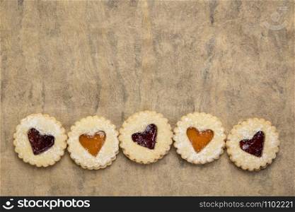 a row of jam heart biscuits on brown handmade textured bark paper with a copy space, dessert or love and romance concept