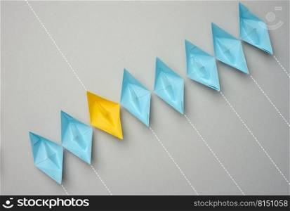 A row of paper boats on a gray background, yellow is moving in the opposite direction. Uniqueness of personality, individuality and independence from another opinion