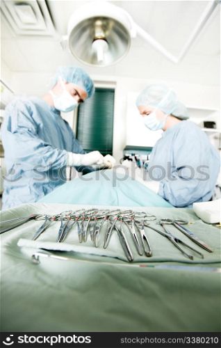 A row of sterile surgery instruments with live surgery being performed in the background