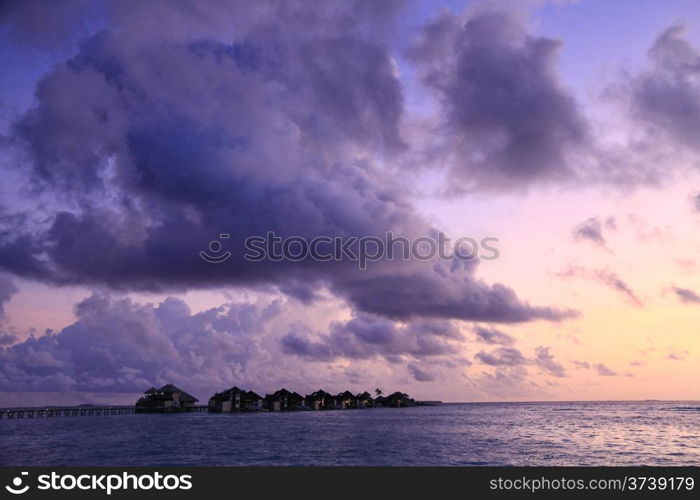 A row of water villas at Gili Lankanfushi (formerly Soneva Gili) against a purple sunset in the Maldives