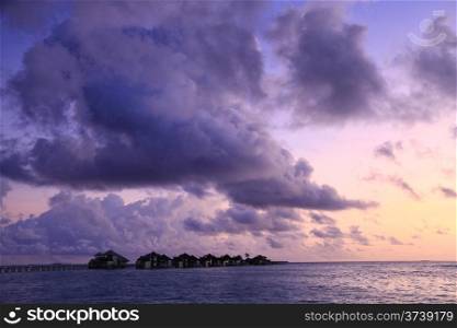 A row of water villas at Gili Lankanfushi (formerly Soneva Gili) against a purple sunset in the Maldives