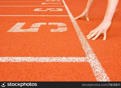 A runner crouches in the &rsquo;start&rsquo; position. Only the hands are viewable, and the image is in profile. Horizontally framed shot.