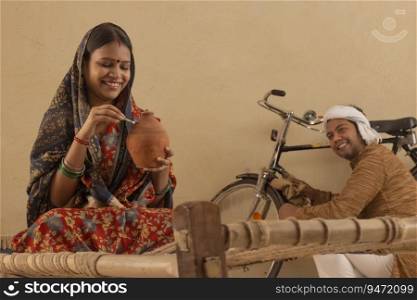 A RURAL HUSBAND HAPPILY LOOKS AT WIFE PUTTING MONEY IN PIGGY BANK