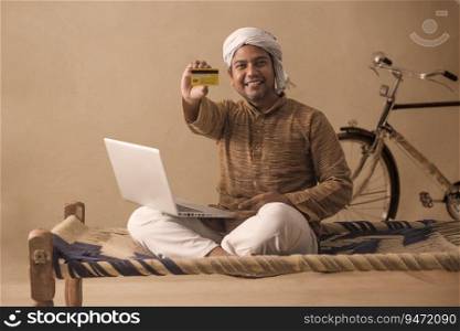 A RURAL MAN SITTING WITH LAPTOP AND SHOWING DEBIT CARD 