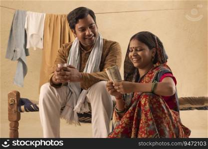 A RURAL WIFE HAPPILY COUNTING MONEY WHILE HUSBAND DRINKS TEA