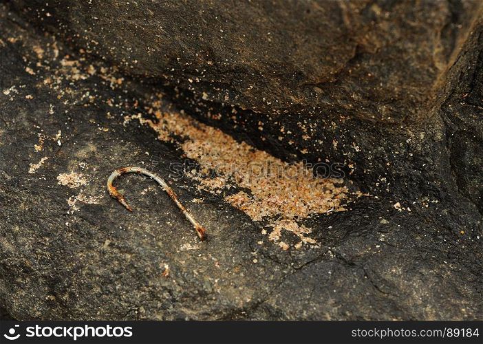 A rusty fish hook on a rock at the seaside