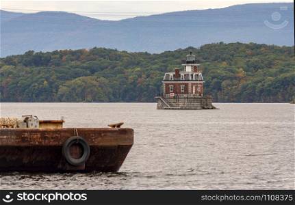 A rusty old barge sits in the foreground near the Hudson Athens Lighthouse in Upstate New York USA