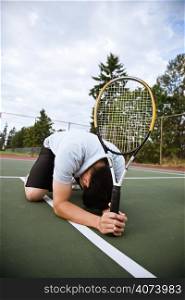 A sad asian tennis player kneeling down in disappointment after defeat