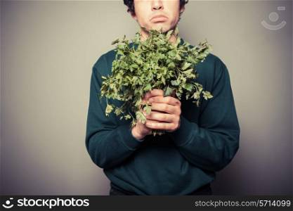 A sad young man is holding a big bunch of parsley