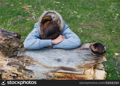 A sad young woman is resting her head on a tree trunk in the park