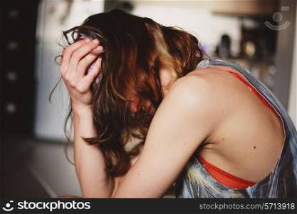 A sad young woman is sitting in her kitchen with a headache