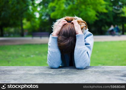 A sad young woman with her head in her hands at a table in the park