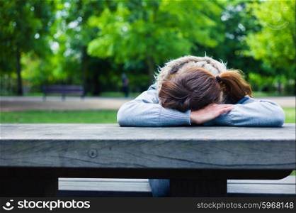 A sad young woman with her head resting on her hands at a table in the park