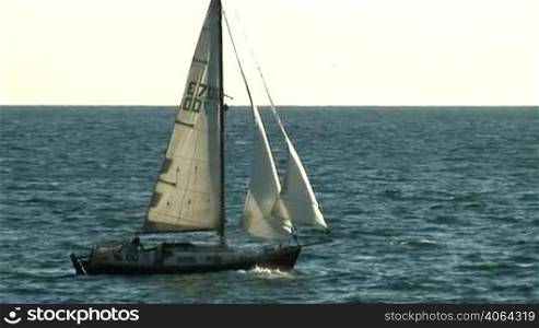 A sailboat cruises slowly over the sea.