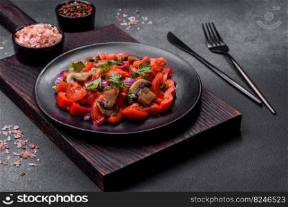 A salad of baked mushrooms, tomatoes, onions, parsley, spices and herbs on a black plate against a dark concrete background. Vegetarian cuisine dish. A salad of baked mushrooms, tomatoes, onions, parsley, spices and herbs