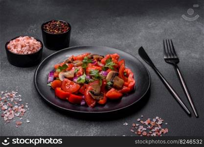 A salad of baked mushrooms, tomatoes, onions, parsley, spices and herbs on a black plate against a dark concrete background. Vegetarian cuisine dish. A salad of baked mushrooms, tomatoes, onions, parsley, spices and herbs