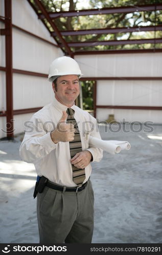 A satisfied construction inspector holding blueprints and giving a thumbsup.