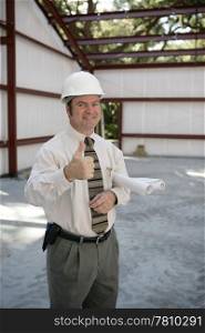 A satisfied construction inspector holding blueprints and giving a thumbsup.