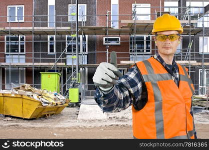 A satisfied looking construction worker giving a thumbs-up in front of a huge residential building site