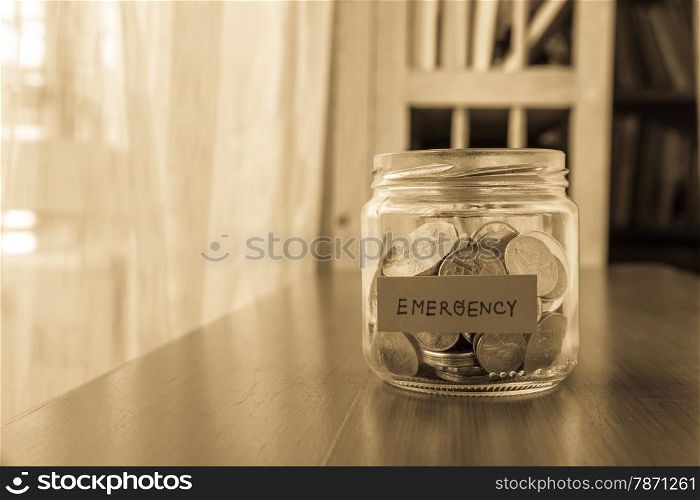 A savings money jar with world coins and emergency word on label or tag